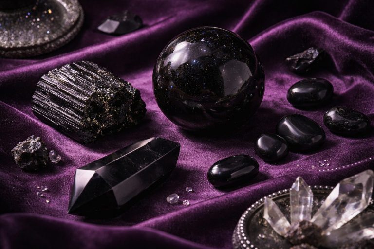 Cristaux noirs élégants — sphère d’obsidienne, tourmaline brute et onyx poli — disposés sur un tissu violet profond, éclairage doux avec ombres marquées, ambiance mystique et luxueuse.